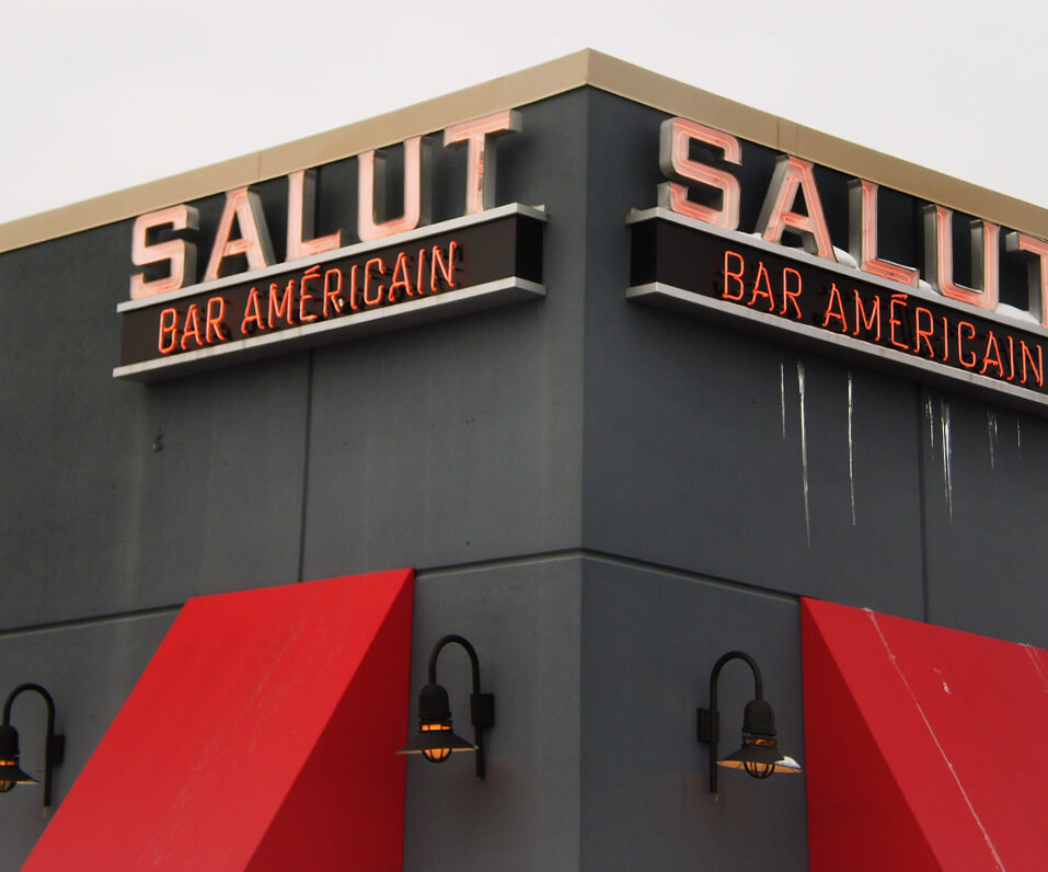 Salut Bar neon channel letters installed on corner of building with red awnings